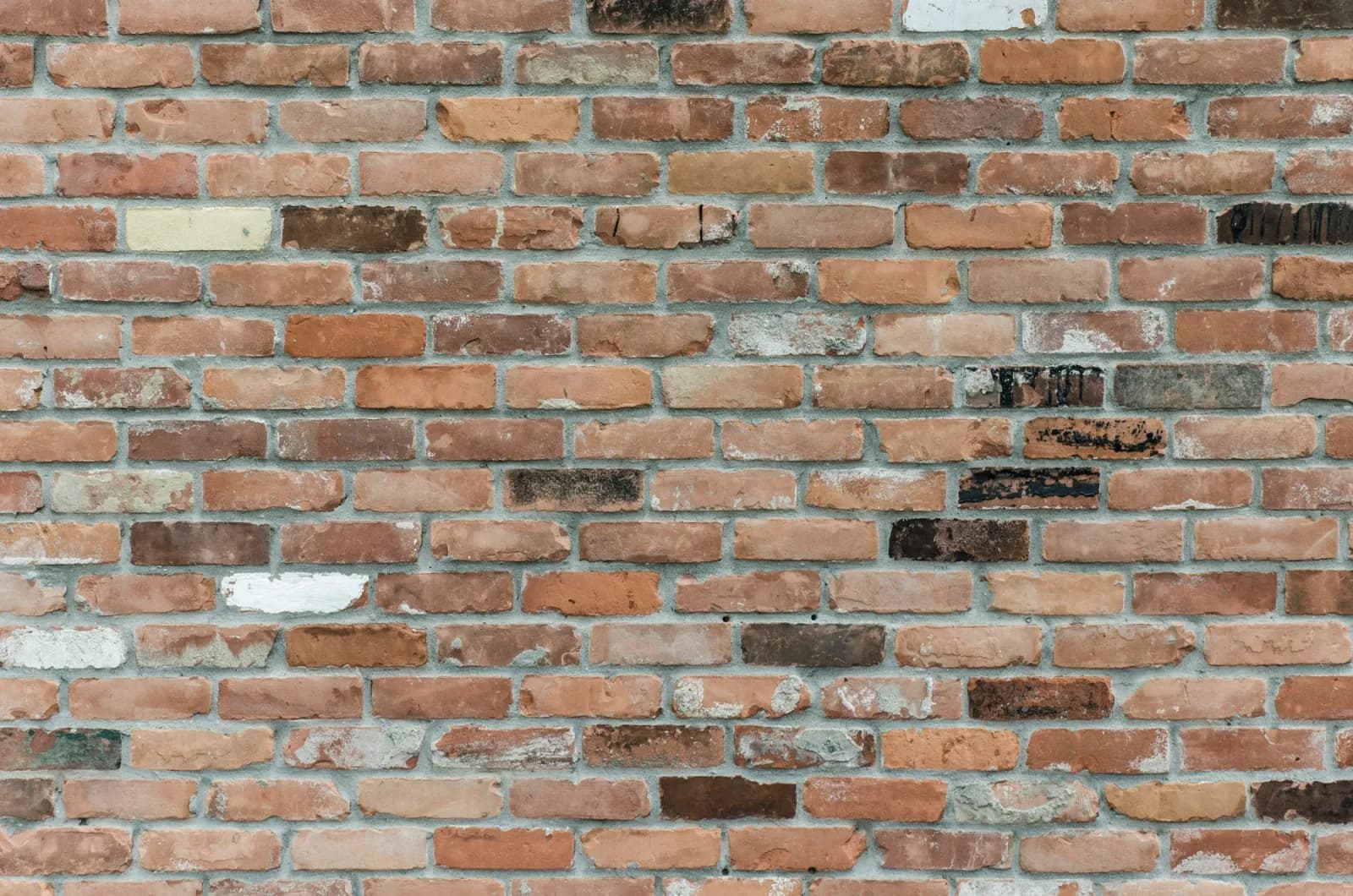 Gammel mur af røde og brune teglsten med slidte mørtelfuger