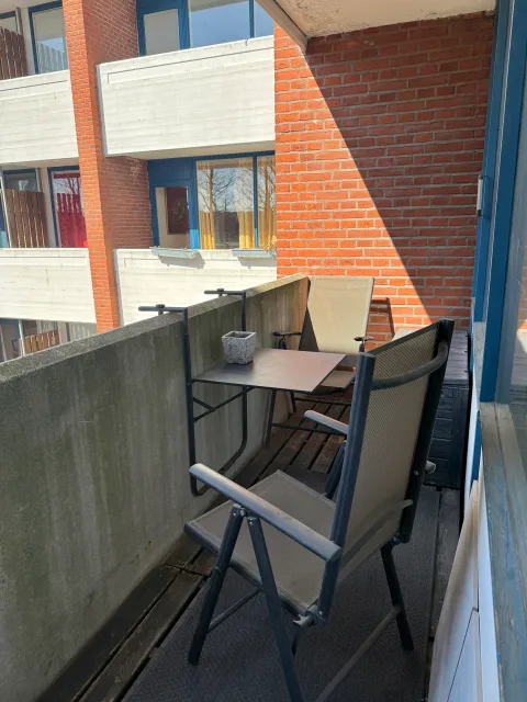 Altanen med bord og to klapstole op ad den røde murstensfacade.
