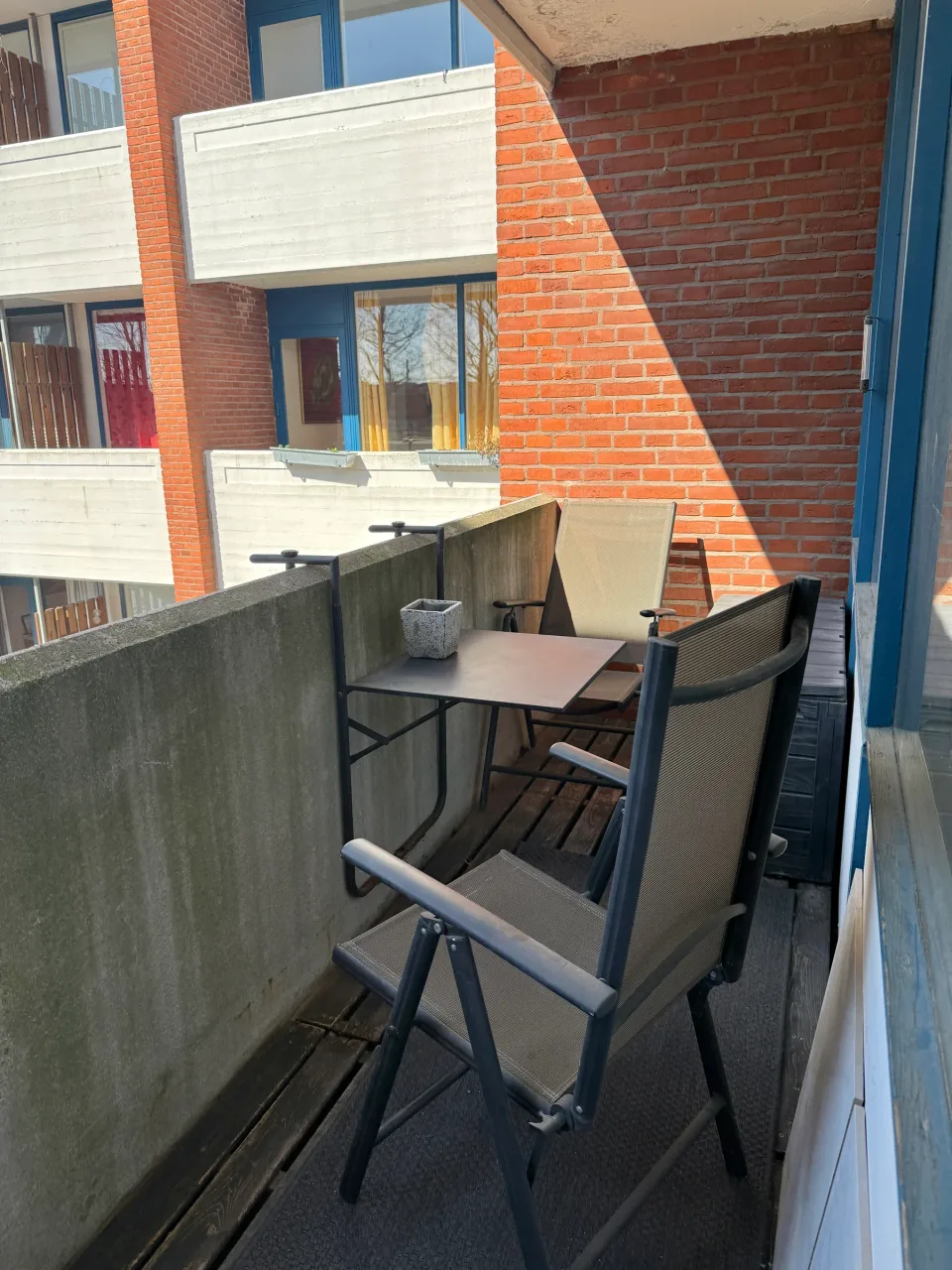 Altanen med bord og to klapstole op ad den røde murstensfacade.