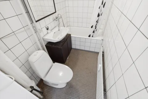 Toilet og håndvask på et mørkt skab i det gamle badeværelse med badekar ved siden af.